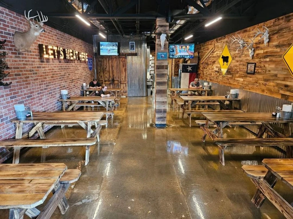 Wide view of the rustic dining area inside Strouderosa BBQ with long wooden tables.