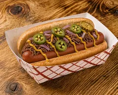 The Hot Dogerosa in a red and white checked paper boat, a smoked hot dog under chopped brisket, pickled jalapeño slices, red onion and zigzags of yellow mustard