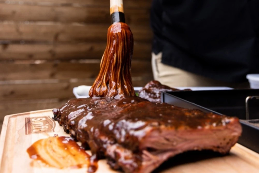 A rack of ribs being mopped with barbecue sauce